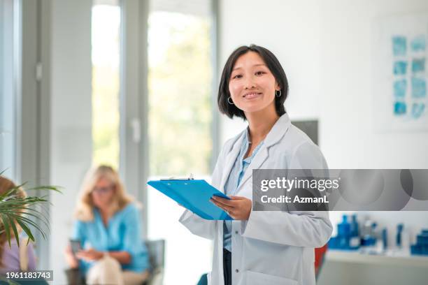 médico asiático adulto medio con portapapeles - bata de laboratorio fotografías e imágenes de stock