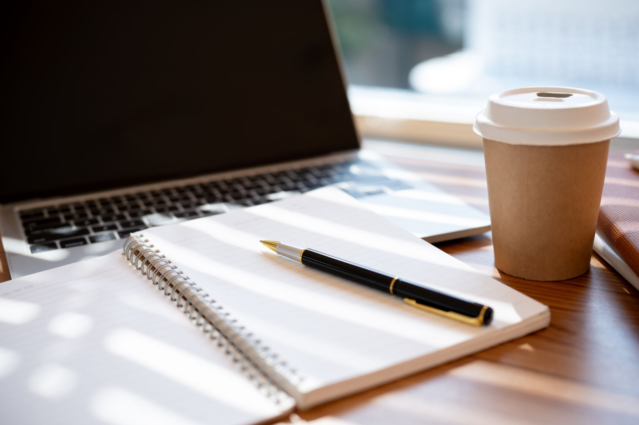 A wooden table with an opened book, a pen, a laptop, and a coffee cup. workspace in a cafe concept A wooden table with an opened book, a pen, a laptop, and a coffee cup. workspace in a cafe concept