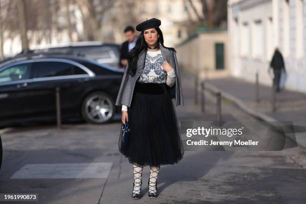 Tina Odjaghian seen wearing black beret hat, silver earrings, silver necklace, white and navy blue butterfly print pattern sweater, white and black...