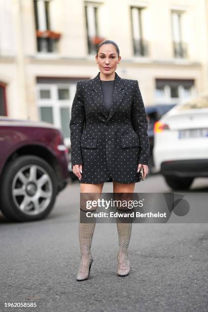 Guest wears a black top, a black oversized blazer jacket with printed white polka dots, knee high shiny boots, outside Viktor & Rolf, during the...