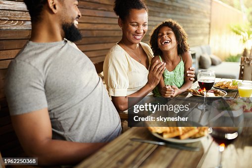 Happy black family talking during a meal at picnic table on a patio. Happy black family talking during a meal at picnic table on a patio.