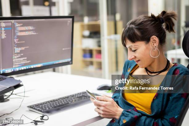 modern workspace where a female developer takes a moment to check her phone amidst coding - hackathon stock pictures, royalty-free photos & images