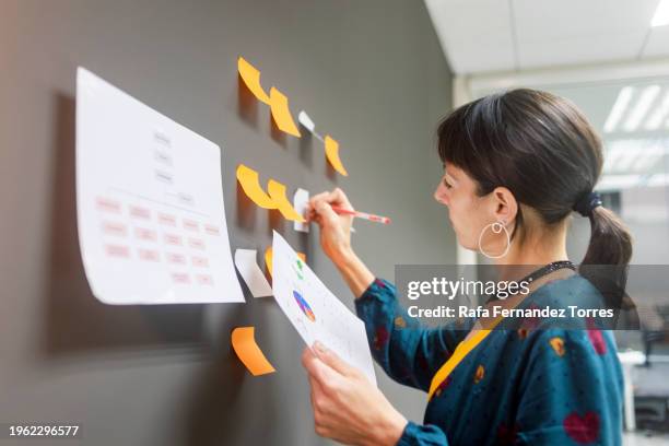 a woman standing in an office looking at pieces of paper pinned on a wall. - mind map stock pictures, royalty-free photos & images