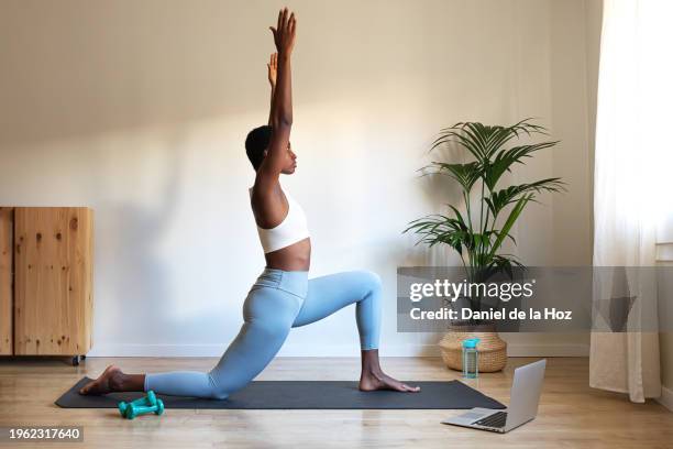 young african american woman doing low lunge yoga pose at home with online tutorial using laptop. anjaneyasana home yoga practice. - tutorial fotografías e imágenes de stock