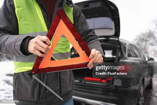 hombre irreconocible, montando una señal de triángulo de advertencia, durante una avería de un vehículo en la carretera en un clima frío invernal - triángulo-de-advertencia fotografías e imágenes de stock