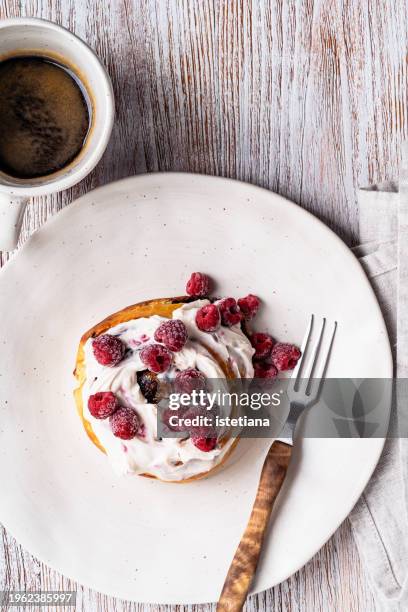 cinnamon roll with cream cheese icing and frozen raspberries, mug of fresh coffee - sticky bun stock pictures, royalty-free photos & images