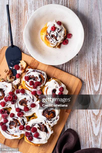 cinnamon rolls with cream cheese icing and frozen raspberries - sticky bun stock pictures, royalty-free photos & images