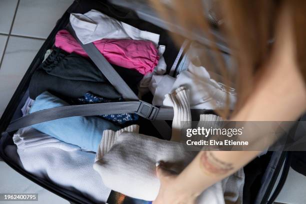 over the shoulder view of a teenager packing folded clothes into a suitcase. - teen packing suitcase stock pictures, royalty-free photos & images