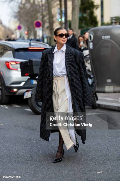 Darja Barannik wears black white striped coat, beige skirt, white button shirt, tights, sunglasses, earrings, heels, Prada bag in brown outside...