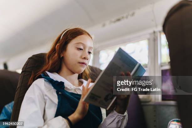 child girl reading a book on school bus - young girl reading book bus foto e immagini stock