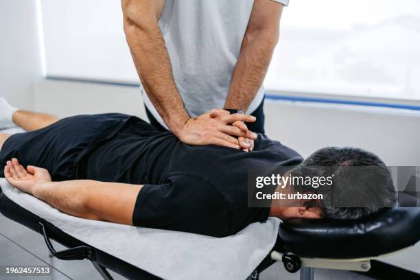 chiropractor adjusting his male client's upper back in his office - chiropractic stock pictures, royalty-free photos & images