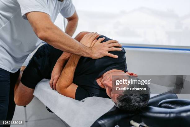 chiropractor adjusting his male client's lower back in his office - chiropractor stockfoto's en -beelden