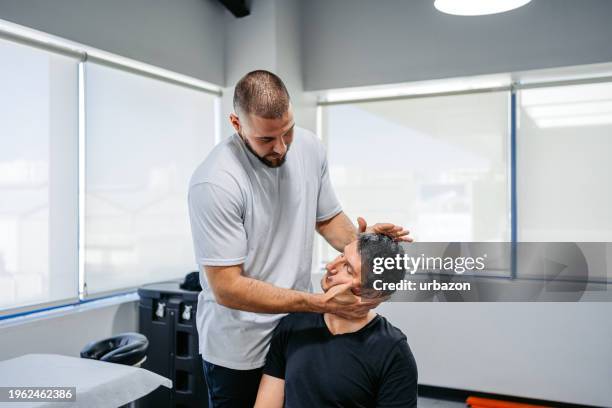 physical therapist adjusting his male client's neck in his office - sports head injuries imagens e fotografias de stock