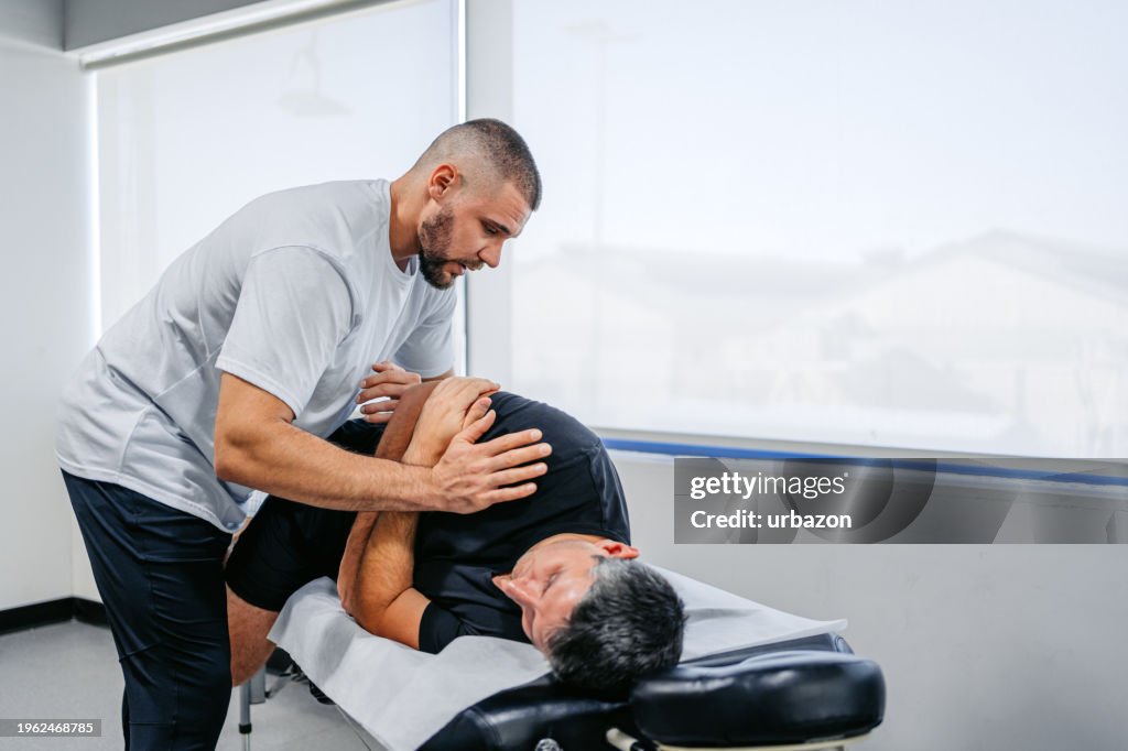 Chiropractor Adjusting His Male Client's Lower Back In His Office