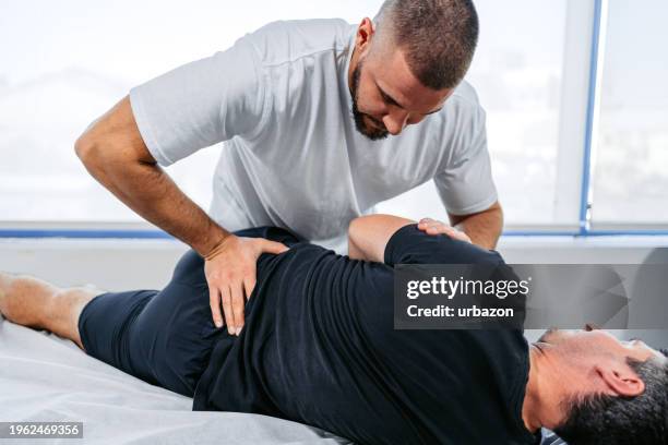 chiropractor adjusting his male client's lower back in his office - chiropractic office stock pictures, royalty-free photos & images