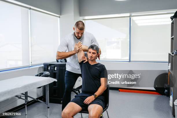 physical therapist adjusting his male client's arm in his office - sjukgymnast bildbanksfoton och bilder