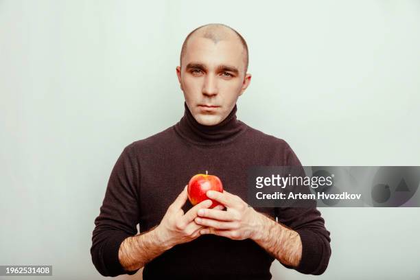 blad haired man  holds a vibramt red-colroed apple fruit. confident look - blad stock pictures, royalty-free photos & images