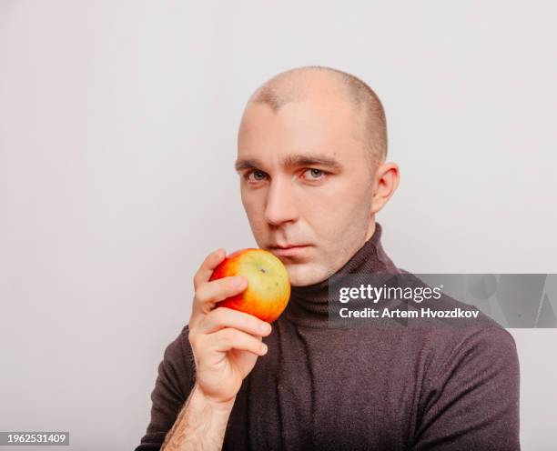 blad haired man  holds a vibramt red-colroed apple fruit. confident look - blad stock pictures, royalty-free photos & images