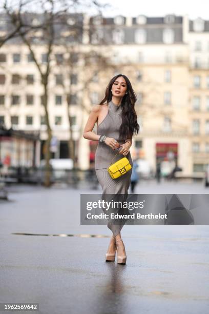 Heart Evangelista wears a sleeveless gray wool ribbed turtleneck long top, a matching midi skirt, the pair forming a long dress, bracelets, a yellow...