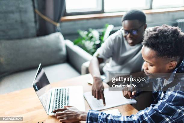 two young adult black male students doing homework using laptop - male student wearing glasses with friends stock-fotos und bilder