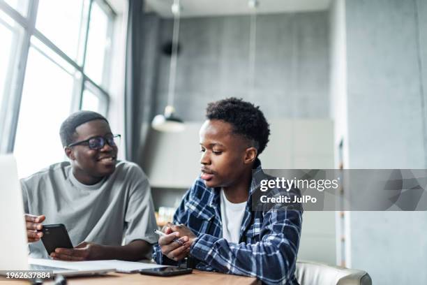 two young adult black male students doing homework using laptop - male student wearing glasses with friends stock-fotos und bilder