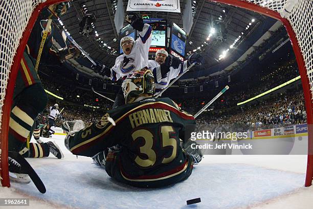 Goalie Manny Fernandez of the Minnesota Wild sits in his crease as Matt Cooke and Trevor Linden of the Vancouver Canucks celebrate a game tying goal...