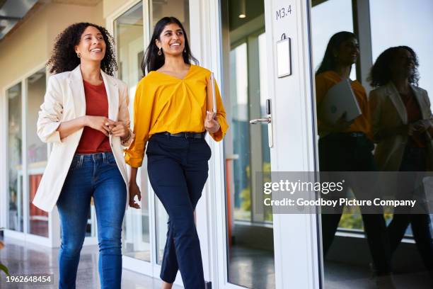 two diverse businesswomen smiling while walking in an office hallway - corporate modern office bright diverse imagens e fotografias de stock