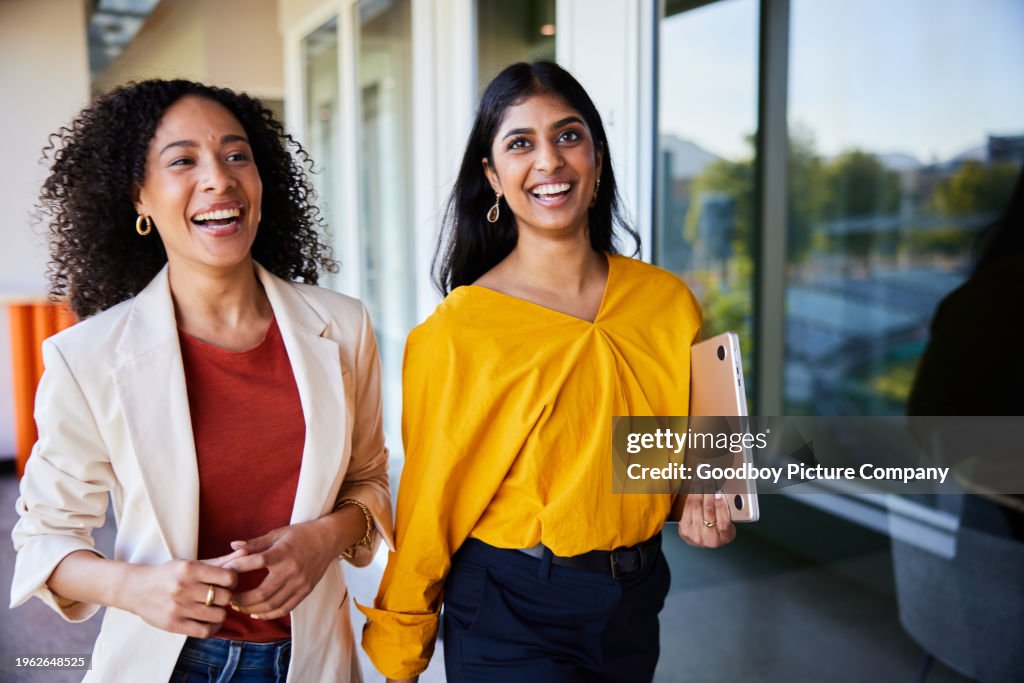 Diverse young businesswomen laughing together while walking in an office
