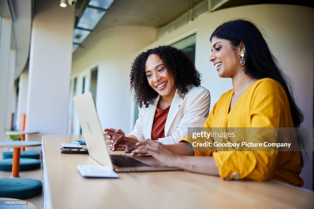 Two businesswomen smiling and working on a laptop at an office table