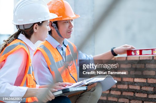 Using Digital Technology Enhances Quality Assurance in Your Construction Project. A female project leader and male engineer use the level tool measuring brick walls to meet a reasonable standard on a construction site.