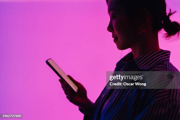 side view of young asian woman in silhouette using smartphone against illuminated magenta screen - mobile billboard stock pictures, royalty-free photos & images