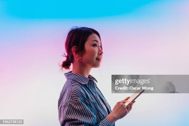 side view of confident young asian woman using smartphone against illuminated gradient screen - computer network stock pictures, royalty-free photos & images