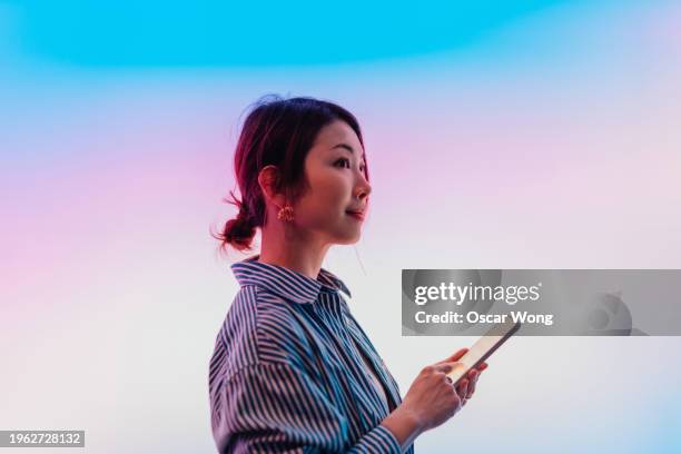 side view of confident young asian woman using smartphone against illuminated gradient screen - mobile billboard stock pictures, royalty-free photos & images