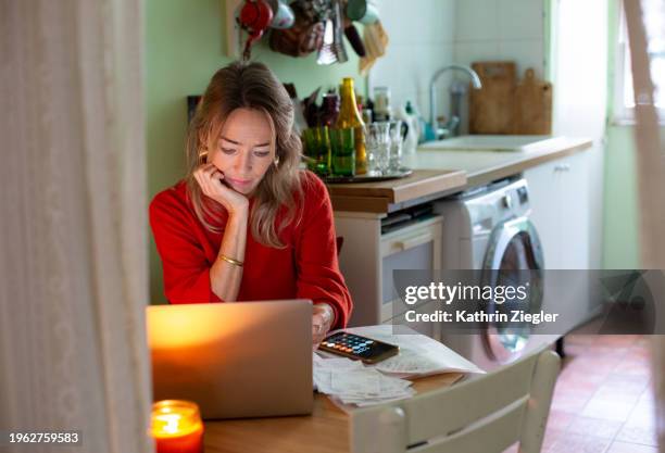woman sitting at kitchen table, using laptop and sorting through paperwork - home office stock pictures, royalty-free photos & images