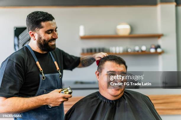 barbiere che taglia i capelli dei clienti dell'uomo maturo al barbiere - negozio del barbiere foto e immagini stock