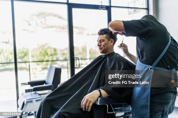 mid adult man getting his hair cut and talk with the barber at barber shop - haar knippen stockfoto's en -beelden