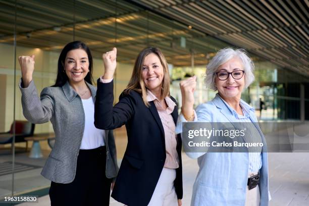 three mature businesswomen flexing their biceps while looking at the camera cheerfully in favor of equality. - frauenpower stock-fotos und bilder
