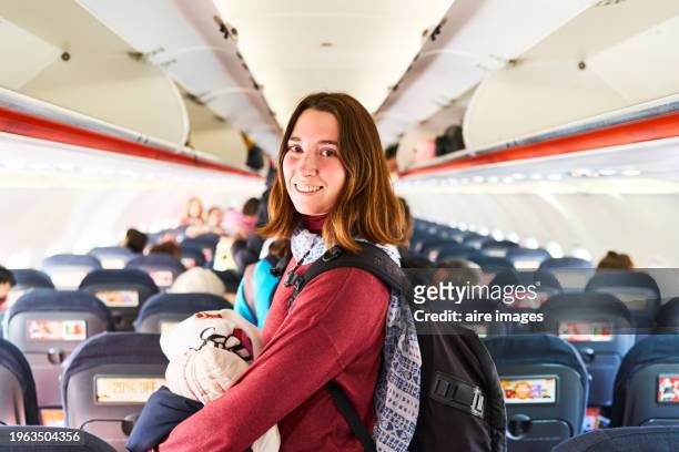 portrait of a beautiful tourist woman in casual clothes and backpack standing inside an airplane hugging a pillow looking at the camera, side view - plane seat stock pictures, royalty-free photos & images