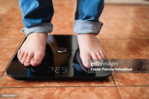 weight management: woman steps onto scale with tape measure, determined to track progress after meal. serious dieting concept - obesidad fotografías e imágenes de stock