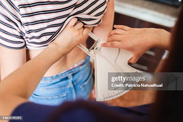 unrecognizable dietitian nutritionist woman doing  back skin fold measurements, subcutaneous body fat with a caliper to a young female patient. high angle view. - skin fold calliper - fotografias e filmes do acervo