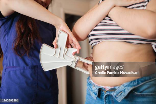 unrecognizable nutritionist professional woman doing abdominal measuring skin fold thickness, subcutaneous body fat with a caliper to a young unrecognizable female patient - skin fold calliper - fotografias e filmes do acervo