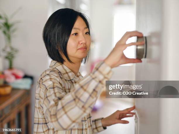 woman adjusting a smart thermostat in a home - thermostat stock pictures, royalty-free photos & images