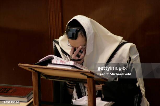 Rabbi with tfillin praying, and with his tallit covering his head during early morning prayers in Yeshiva Gedolah Zichron Moshe Synagogue.