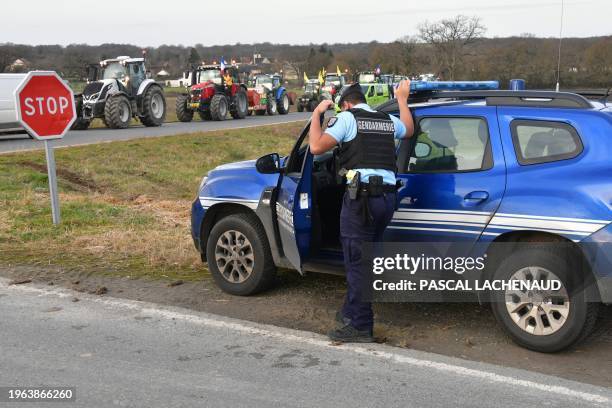 Gendarme stands by his vehicle as tractors run on a road in Vigoux,on January 30 on their way to Rungis wholesale food market amid nationwide...