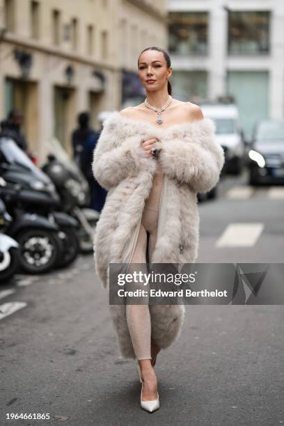 Guest wears a heart-shaped necklace, a white off-shoulder faux fur fluffy long winter coat, mesh leggings, white pointed shoes / pumps, outside...