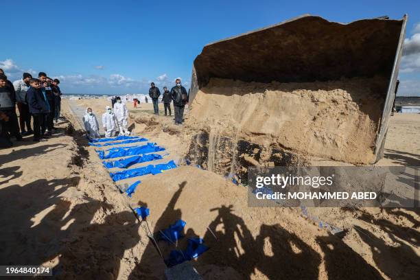 Civilians watch as Gaza-based Palestinian Health Ministry workers bury the bodies of unidentified Palestinians whose date of death is not known after...