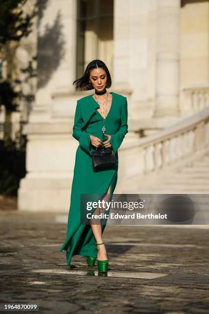 Heart Evangelista wears hair pins, a choker, jewelry necklace, a bold green long slit dress with shoulder pads, a black shiny crocodile leather...