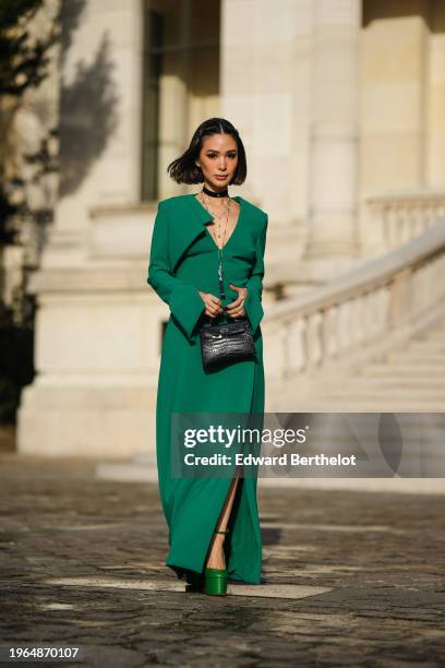 Heart Evangelista wears hair pins, a choker, jewelry necklace, a bold green long slit dress with shoulder pads, a black shiny crocodile leather...