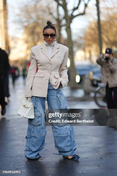 Guest wears sunglasses, earrings, a white turtleneck wool knitted pullover, a white oversized blazer jacket, a white Hermes bag, blue flared cargo...