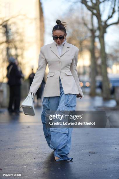 Guest wears sunglasses, earrings, a white turtleneck wool knitted pullover, a white oversized blazer jacket, a white Hermes bag, blue flared cargo...
